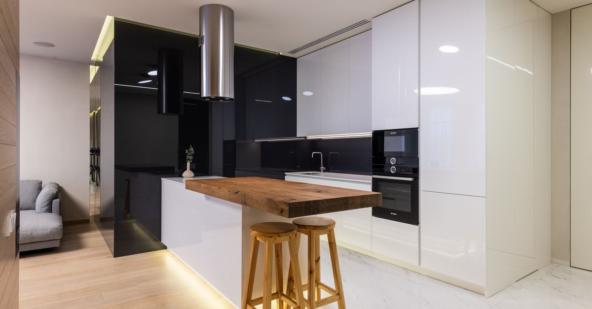 Interior of modern apartment with kitchen zone furnished with glossy cabinets and living area with sofa